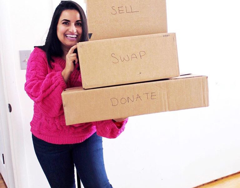 a woman in a pink sweater holding a stack of boxes that say salvage, donate, swap, sell